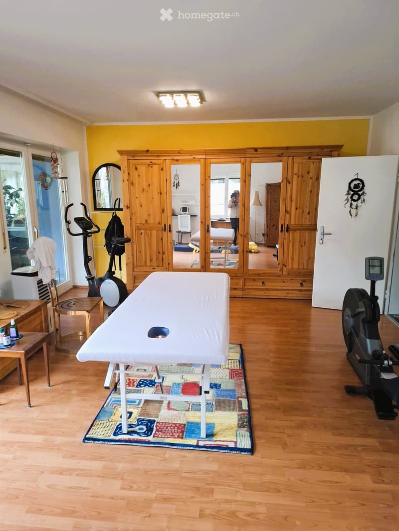 A room with a massage table, exercise equipment, wooden cabinets, and a yellow wall.