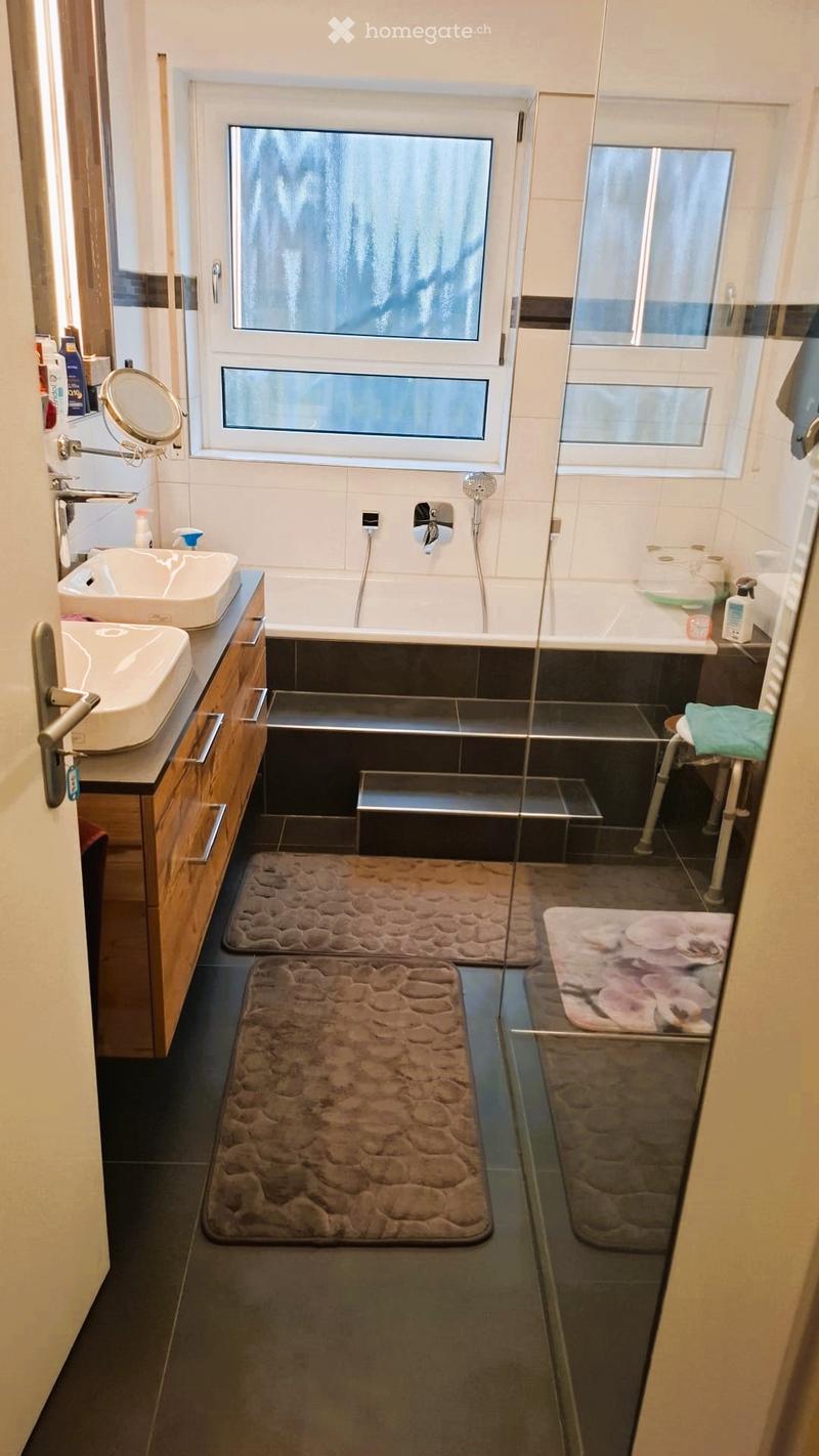 Bathroom with two sinks, a bathtub, a shower, and a toilet. The bathroom has a wooden cabinet, a mirror, and a glass door.