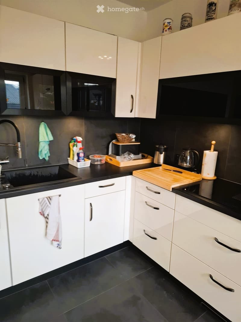 modern kitchen with white cabinets, black countertops, black tiled floor, sink, faucet, microwave, toaster, coffee maker, chopping board, knives, paper towels, cleaning products