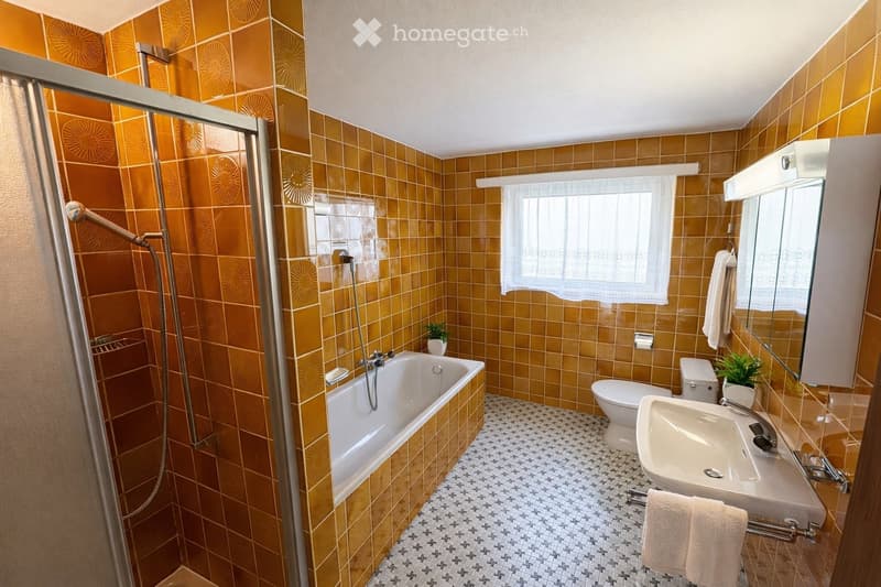 Bathroom with orange tiles, a bathtub, toilet, sink, mirror, and a glass-enclosed shower area.