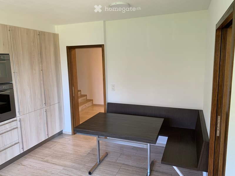 Modern kitchen with light wooden cabinets, a built-in oven, a dark wooden dining table, and a bench seating area.