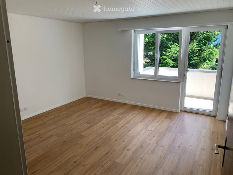Empty room with wooden flooring, white walls, and large sliding glass doors leading to a balcony.