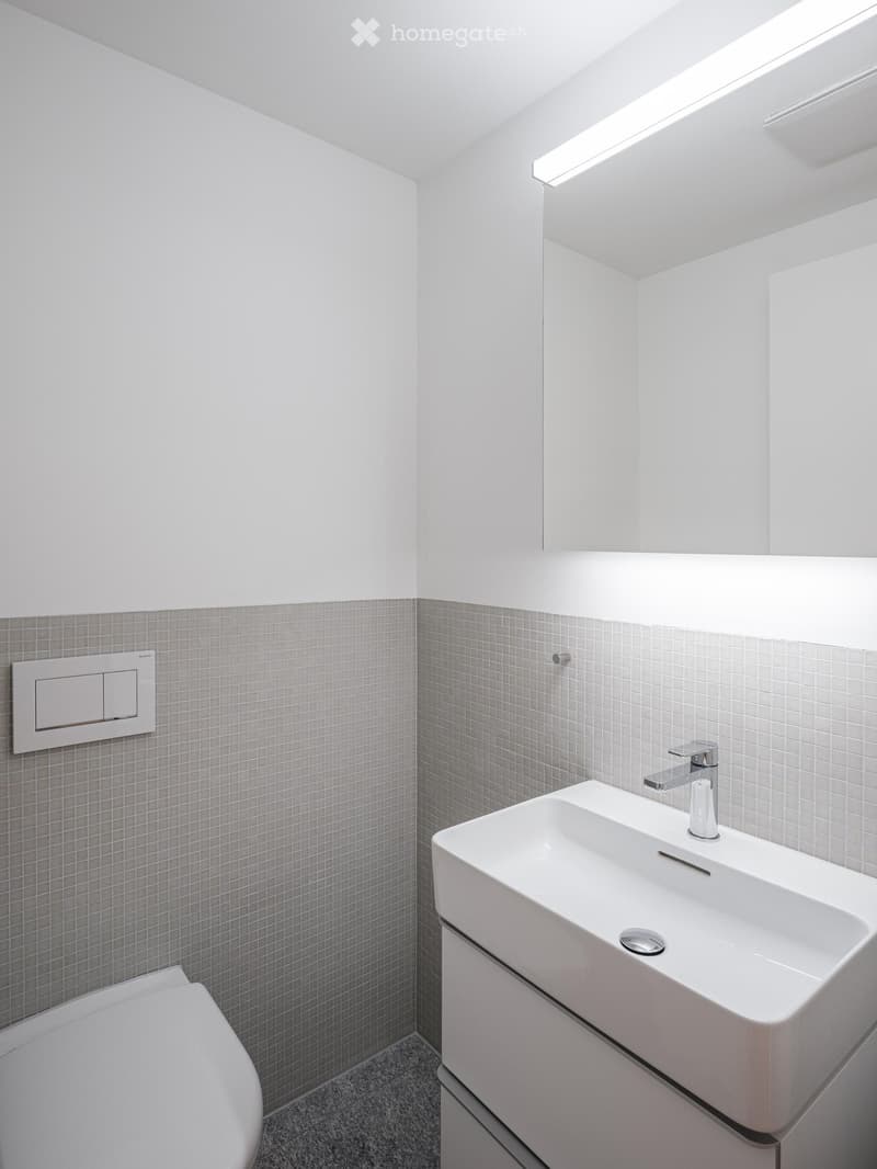 modern bathroom with white tiles, white sink, silver faucet, white toilet, mirror, and white light strip