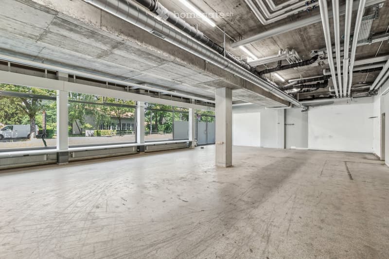 Empty room with concrete floor, large windows, metal pipes on ceiling, benches along the windows.