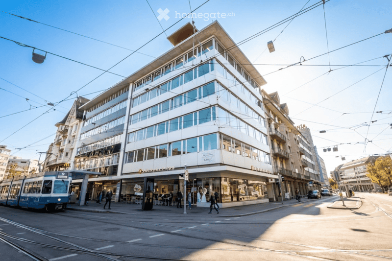 Modern office building with glass facade, multiple floors, located on a busy street with tram tracks and pedestrians.