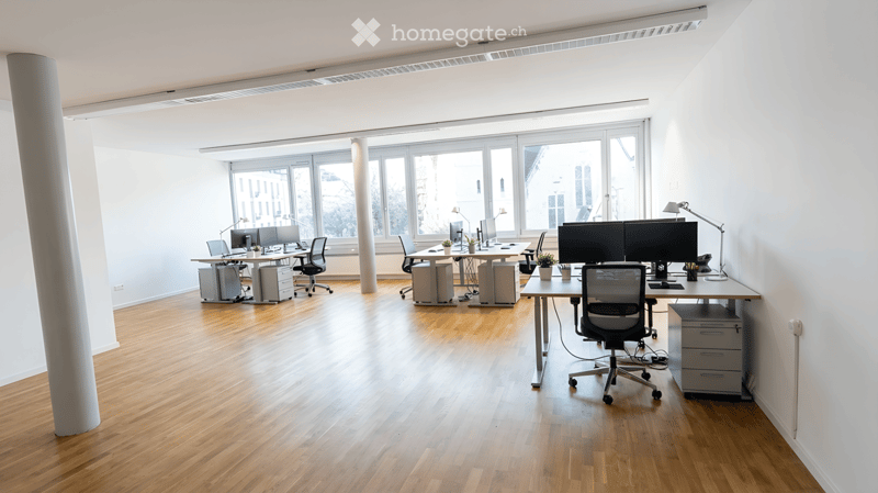Wooden floor, white walls, large windows, office desks, computer monitors, office chairs, lamps
