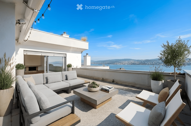 Outdoor seating area with a sofa, coffee table, and chairs, overlooking a lake and mountains.