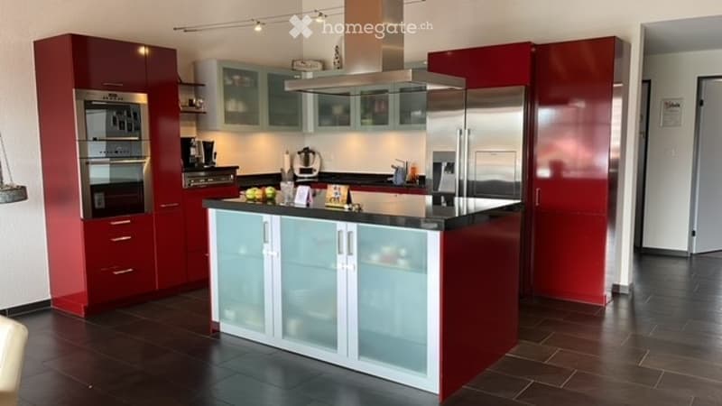 Modern kitchen with red and white cabinets, stainless steel appliances, a central island with a black countertop, and various kitchen items on the counter.