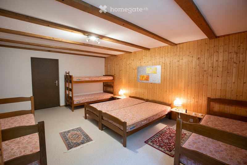 bedroom with four beds, two single beds, and two bunk beds, wooden walls, floor, and bed frames, carpets, lamps, and a small table