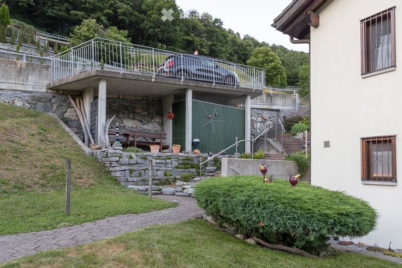 Car park with stairs and railings, wooden bench, decorative objects, green door, large bush, gravel walk way, white building
