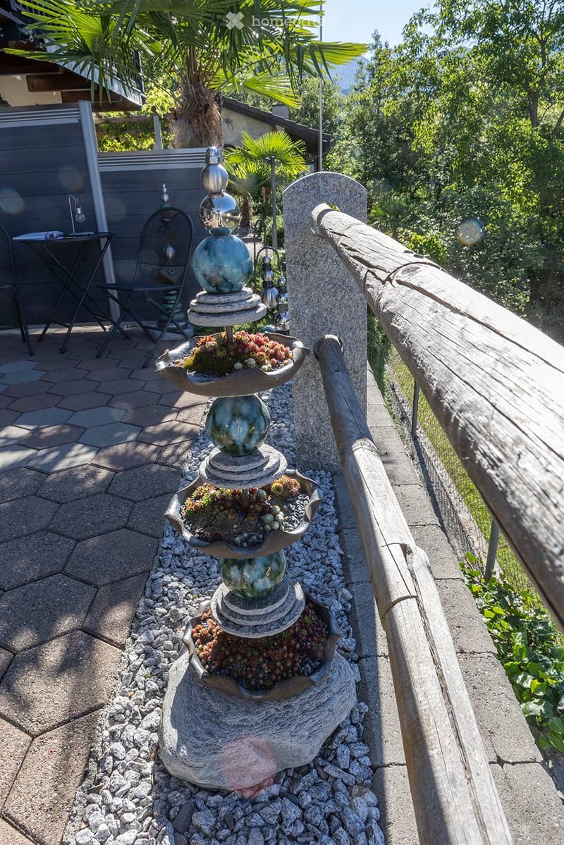 balcony garden with table and chairs, stack of decorative plant pots with rocks and plants, wooden fence, scenic view, greenery