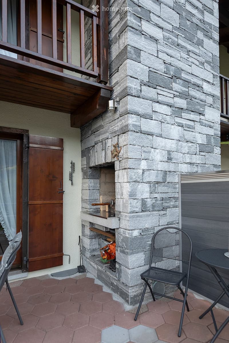 Outdoor fireplace with chimney, surrounded by stone wall, small balcony with wooden railing
