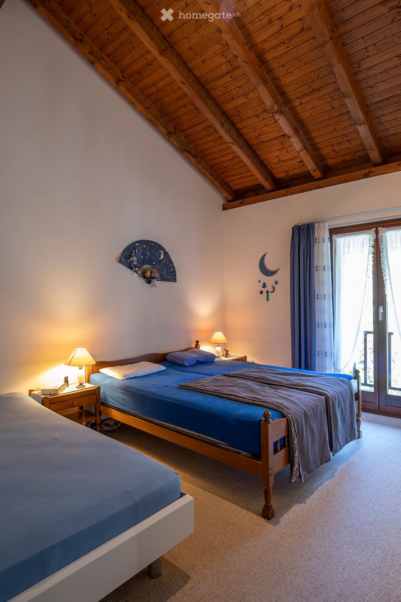 2 beds, blue bedding, nightstands with lamps, fan on wall, sliding glass door to balcony