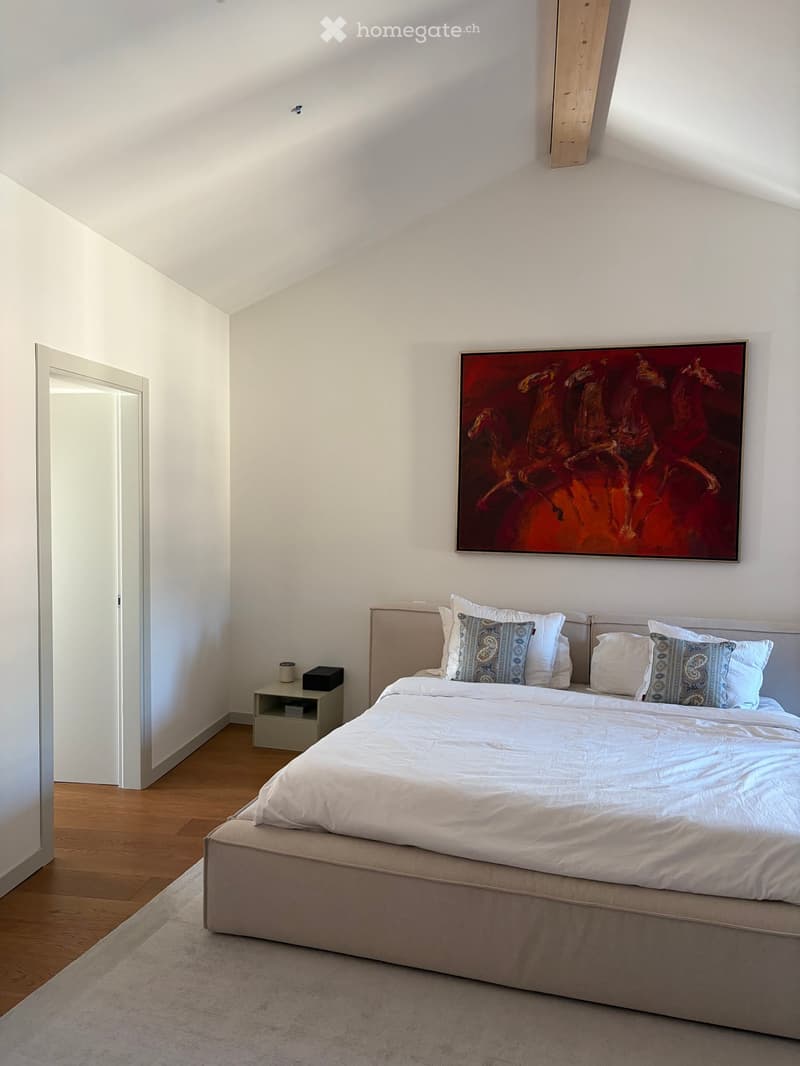 Modern bedroom with a large bed, white bedding, decorative pillows, a nightstand with a lamp, and a large abstract painting on the wall.