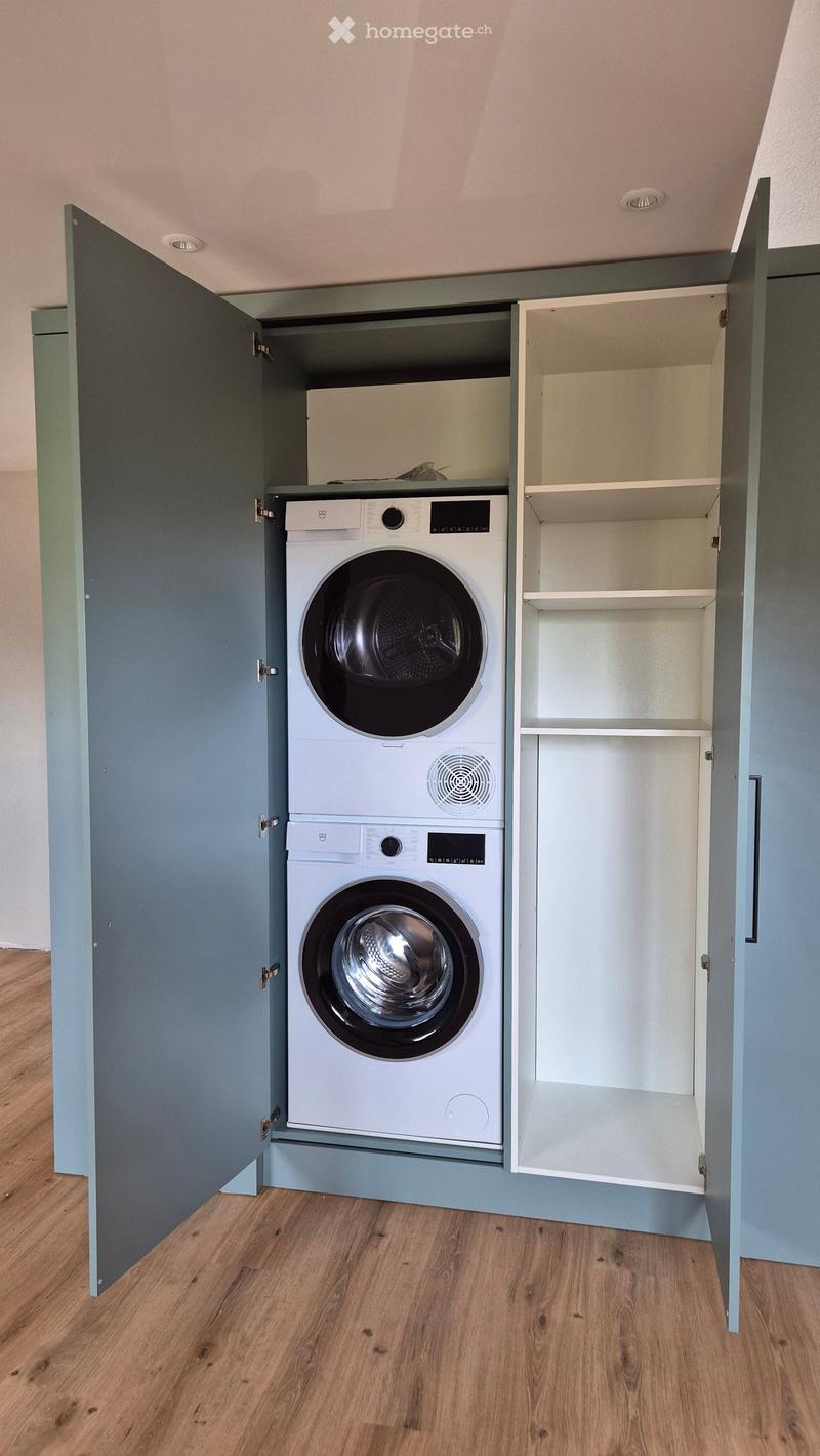 A compact, built-in laundry area with a washing machine and dryer housed within custom cabinetry, featuring light blue paneling and wooden flooring.