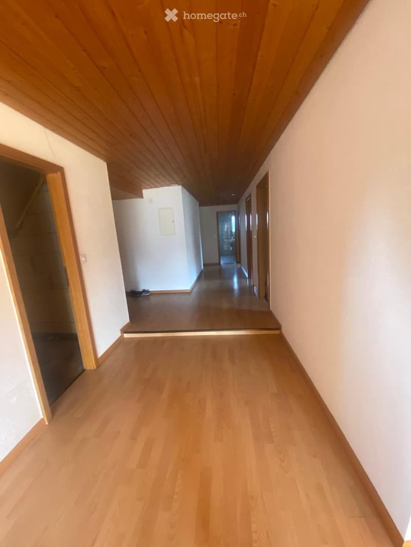 Empty hallway with wooden flooring and white walls, featuring several doors and a light fixture on the wall.
