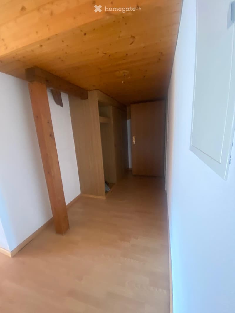 Empty hallway with wooden floor and white walls, featuring a wooden beam support and a closed door at the end.