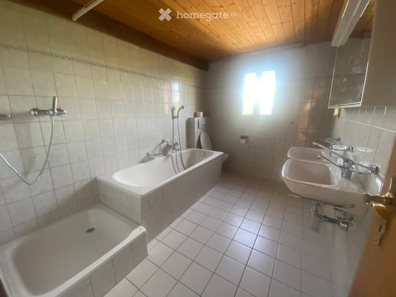 Bathroom with a bathtub, shower, double sink, and toilet. Light-colored tiles and wooden ceiling.
