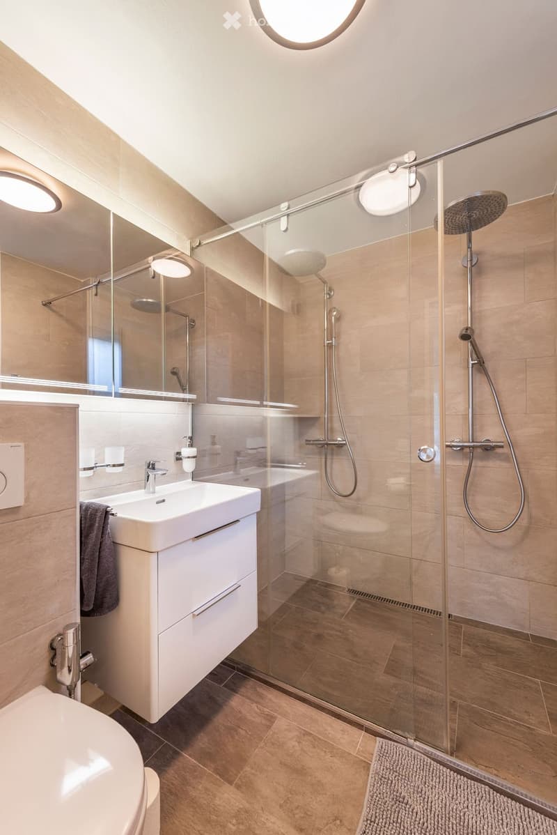 Bathroom. Modern bathroom with a white sink, chrome faucet, large mirror, glass-enclosed shower with multiple showerheads, and a towel hanging on the side.