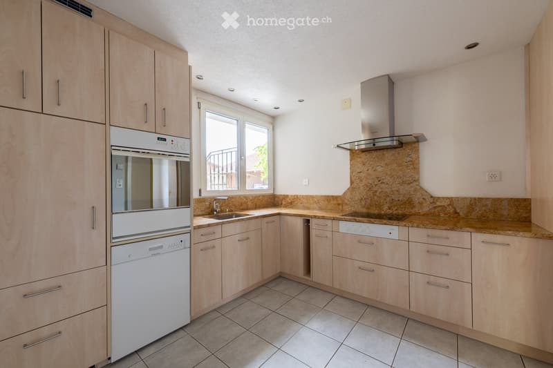 Modern kitchen with light wooden cabinets, stainless steel appliances, and a stone backsplash.