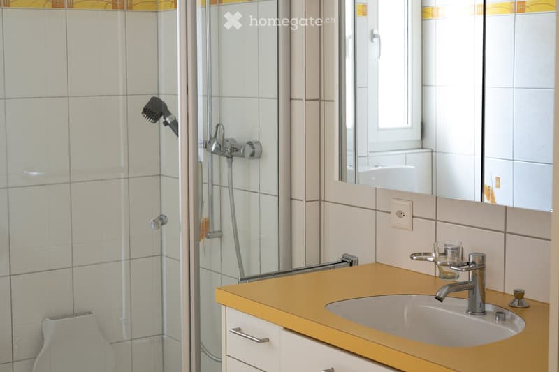 Modern bathroom with a glass-enclosed shower, a white tiled wall, a yellow countertop, a white sink, and a mirror above it.