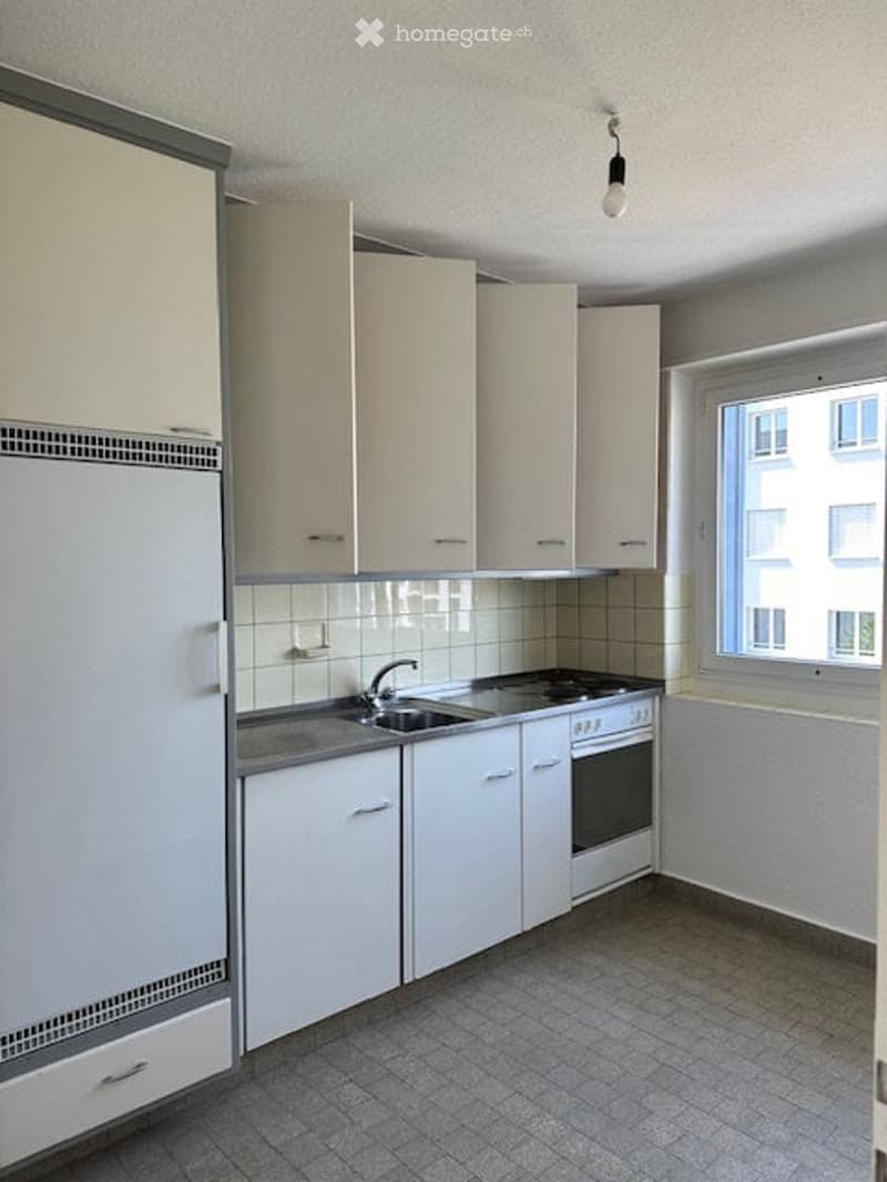 Modern kitchen with white cabinets, stainless steel sink, and oven. The space is clean and organized with tiled flooring and walls.
