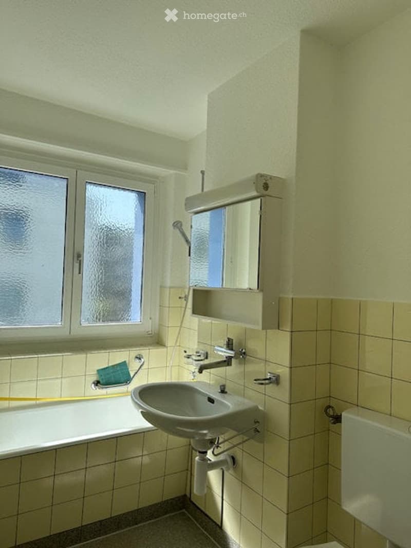 Bathroom with tiled walls and floor, a sink, bathtub, mirror, and showerhead.