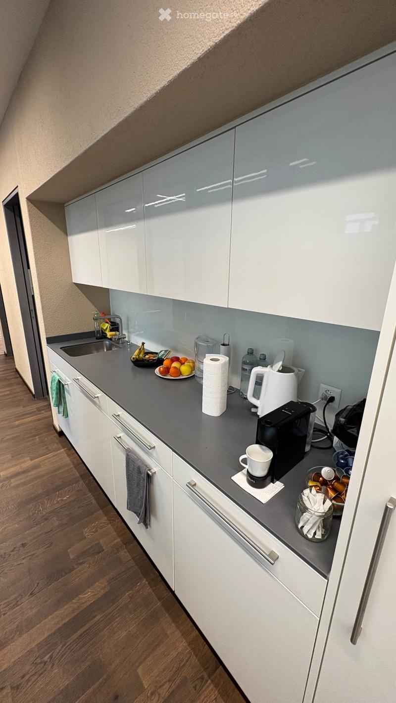 modern kitchen with white cabinets, gray countertop, sink, coffee machine, kettle, plates, fruits, towels, power outlet, wooden floor