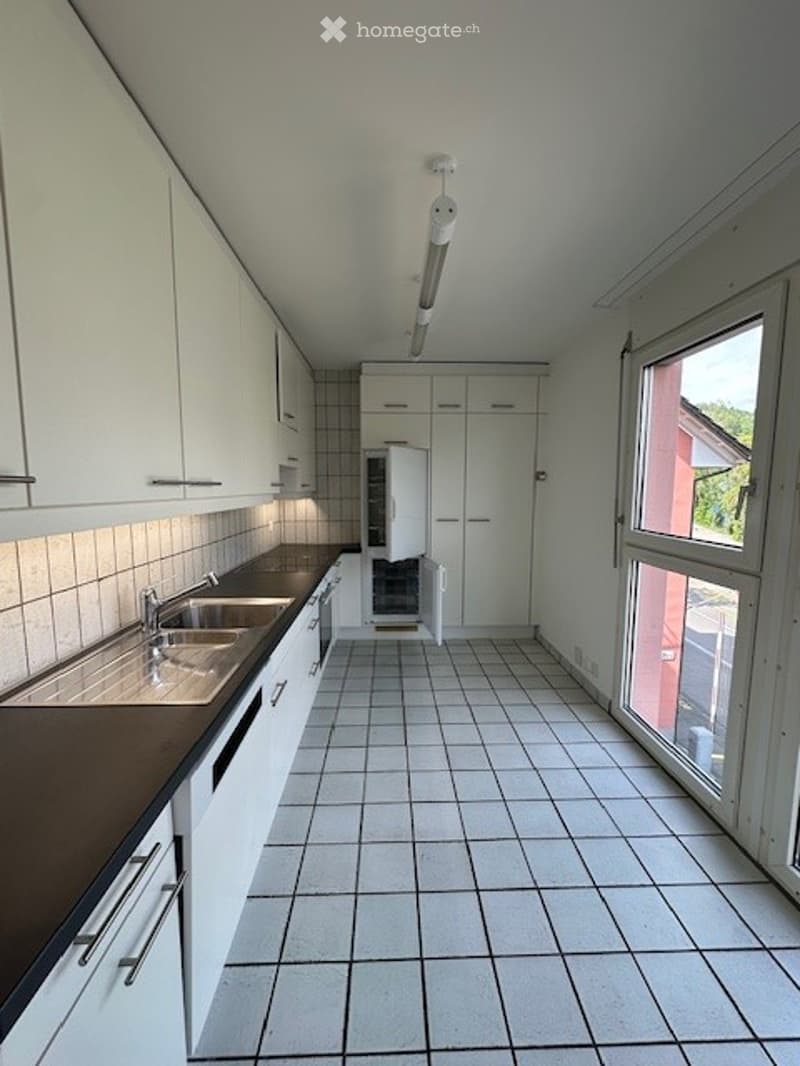 Modern kitchen with white cabinets, tiled floor, and a sink with a faucet. The kitchen is empty and well-lit.