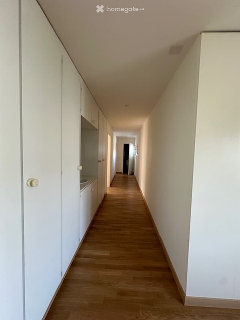 Empty corridor with white walls, wooden floor, and built-in cabinets.