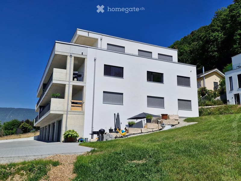 Modern two-story house with white facade, large windows, balconies, and outdoor seating area with umbrella and grill.