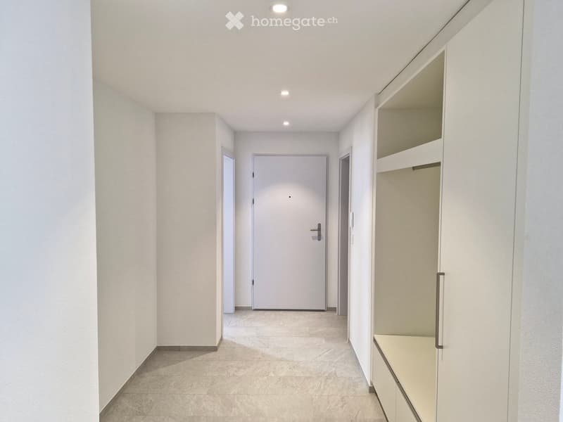Modern, minimalist hallway with white walls, tiled floor, and recessed lighting. Features a built-in closet with open shelving on the right side and a closed door at the end.