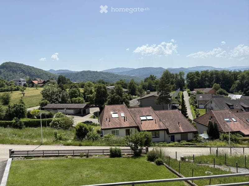 A peaceful suburban neighborhood with houses, trees, and a clear view of distant hills under a bright blue sky.