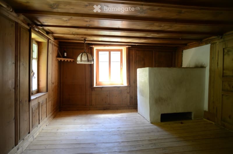 Empty room with wooden walls, ceiling beams, and floor, featuring two windows and a built-in shelf with a bottle on it.