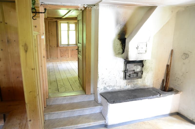 Empty hallway with wooden walls, a stone staircase, and a visible fireplace area with a metal stove and wooden tools.