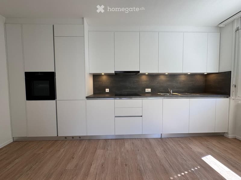 Modern kitchen with white cabinets, stainless steel sink, oven, and wooden flooring.