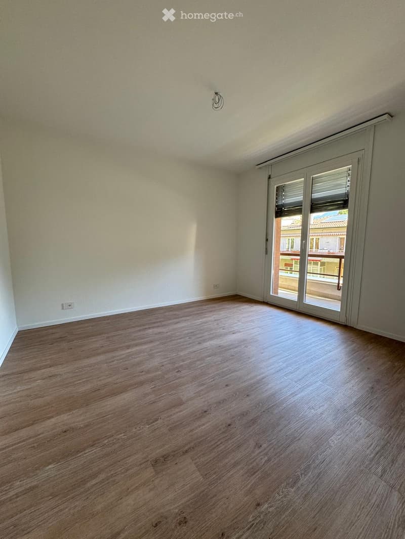 Empty room with wooden flooring, white walls, and a large sliding glass door leading to a balcony.