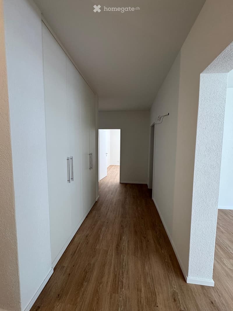 Empty hallway with wooden flooring, white walls, and built-in white cabinets on one side.