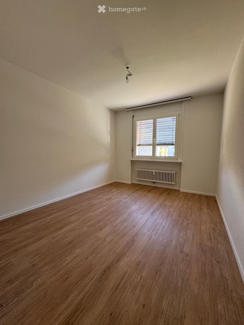 Empty room with wooden flooring, white walls, a window with blinds, and a radiator below the window.