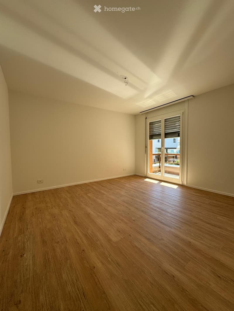 Empty room with wooden flooring, light-colored walls, and a large sliding glass door leading to a balcony.