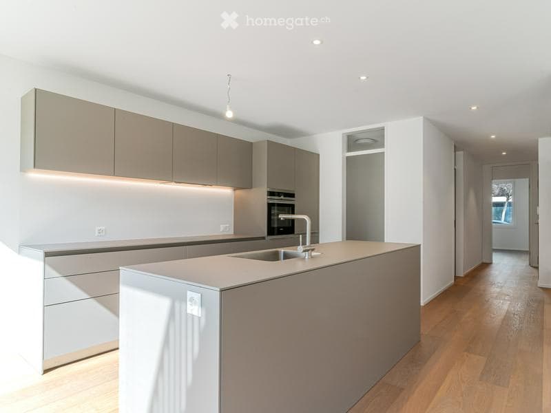 Modern kitchen with light grey cabinets, a central island, and built-in appliances including an oven and sink.