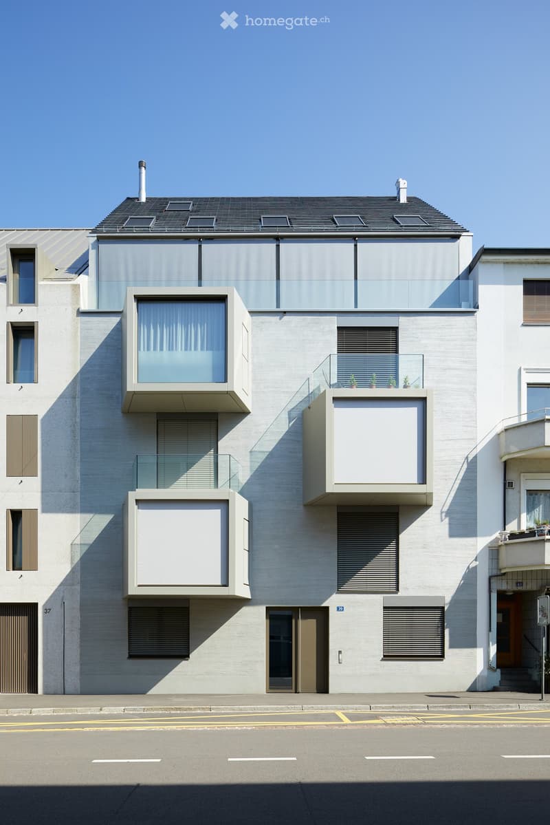 Modern two-story building with clean lines, large windows, and glass balconies. Features a flat roof with skylights and a contemporary design.