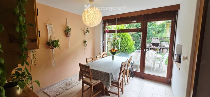 Bright dining area with a table, chairs, vase with flowers, and hanging plants. Large sliding glass doors open to a patio with outdoor furniture.