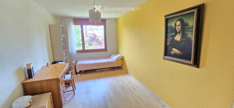 Bright bedroom with wooden flooring, a single bed, a wooden desk, a chair, a large painting, and a window with curtains.