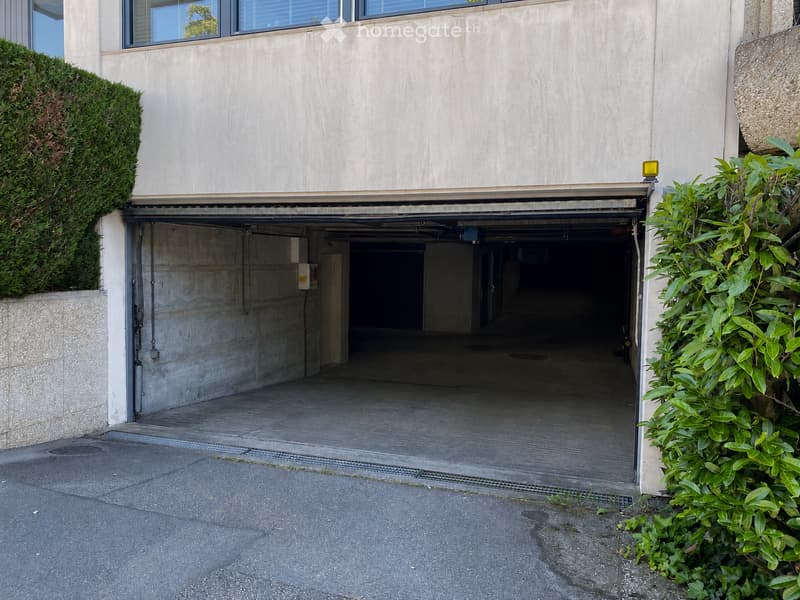 A modern building with a large, open garage entrance, surrounded by greenery and concrete walls.