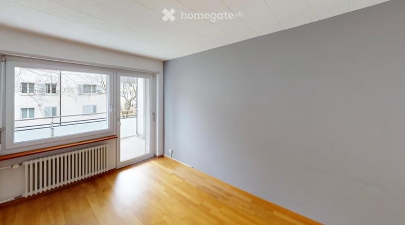 Empty room with wooden flooring, grey walls, large window, and sliding glass door leading to a balcony.