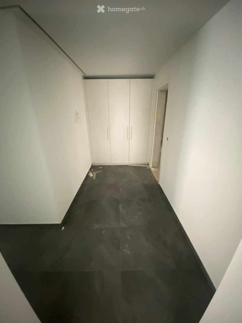 Empty hallway with white walls, black polished floor, and white closet doors at the end.