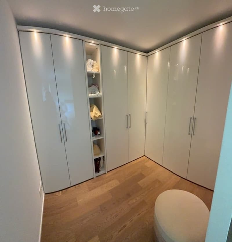 walk-in closet with white cabinets, wooden floor, white ottoman