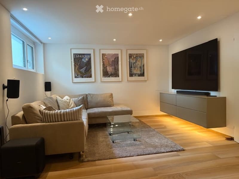open-plan living/dining area, modern design, beige sectional sofa, glass center table, large TV on wall, hardwood floors, speakers