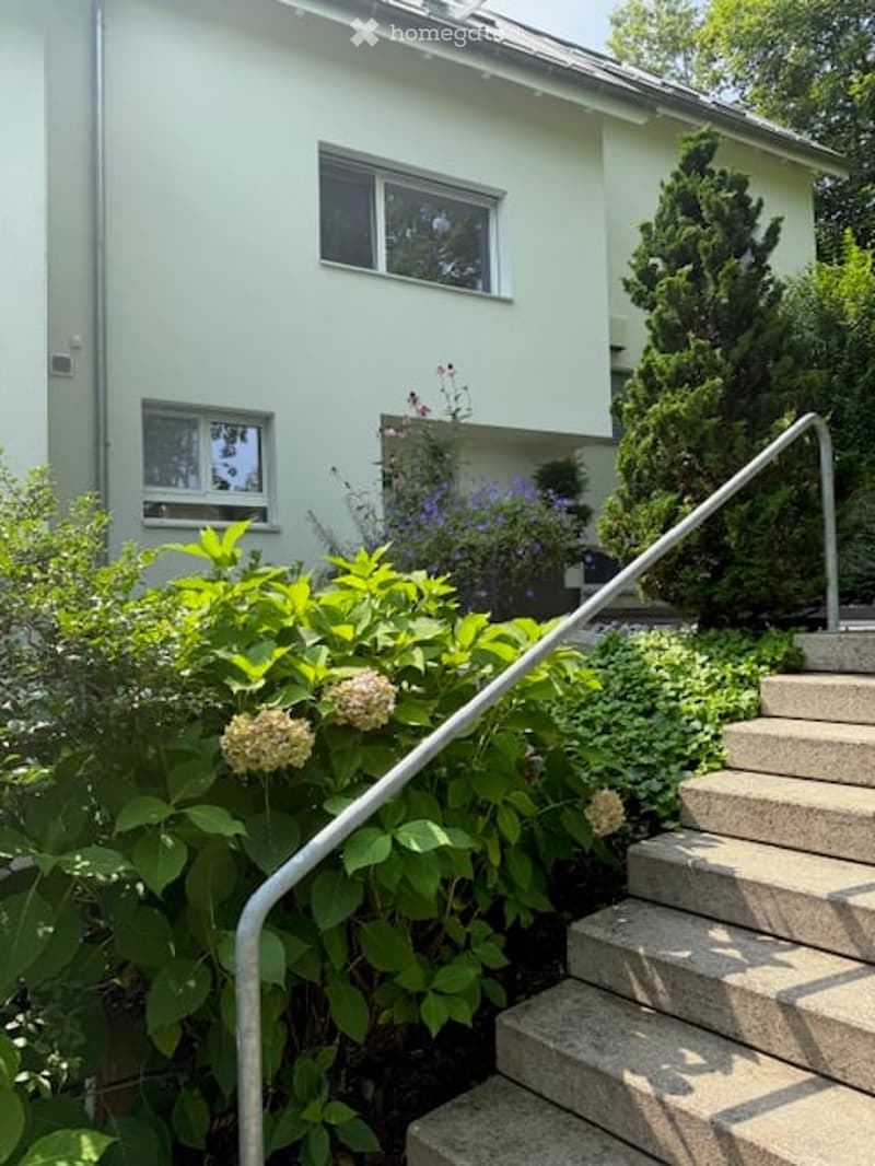 white painted house, raised ground floor, stairs leading to entrance, garden with shrubs and flowers